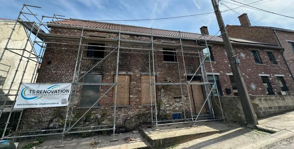 Toiture en tuiles et charpente rénovée à Roux Maison en cours de rénovation à Roux, avec un échafaudage installé pour la pose d'une nouvelle toiture en tuiles. La rénovation inclut également la reconstruction du mur du pignon et l'installation d'une nouvelle charpente, réalisée par TS Rénovation, spécialiste en travaux de toiture dans la région de Charleroi.
