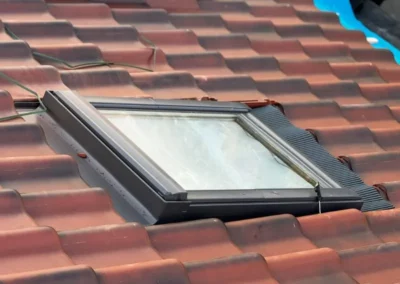 Vélux installé dans une toiture en tuiles récemment rénovée. Le cadre du vélux est bien intégré avec un système d'étanchéité autour pour éviter toute infiltration d'eau, assurant ainsi une protection optimale et l'apport de lumière naturelle.