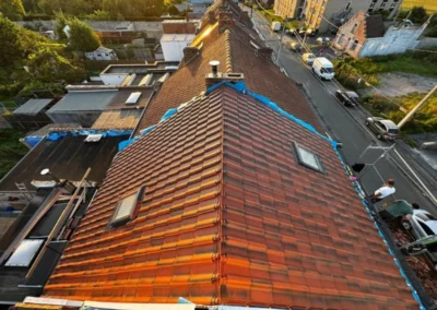 Vue d'ensemble de la nouvelle toiture en tuiles sur une maison. Le toit est recouvert de tuiles rouges, avec deux vélux intégrés pour apporter de la lumière naturelle aux combles. La rénovation assure une parfaite étanchéité et un aspect esthétique harmonieux.