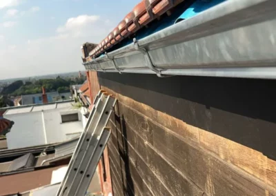 Pose d'une nouvelle gouttière en métal sur une toiture récemment rénovée à Jemappes. La gouttière est fixée sous les tuiles pour assurer une évacuation efficace des eaux pluviales.