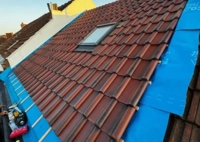 Pose des tuiles sur le lattage et la sous-toiture. Les tuiles sont soigneusement alignées pour assurer une couverture durable et esthétique, avec un vélux intégré pour la lumière naturelle.