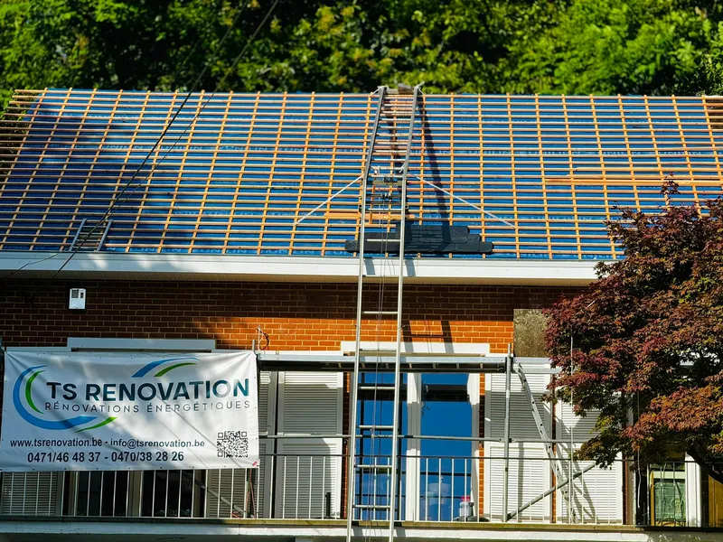 Travaux de rénovation de toiture en cours sur une maison en brique rouge. Pose de lattage et contre-lattage sur une sous-toiture isolante, méthode d'isolation type sarking pour améliorer l'efficacité énergétique. Une bannière de l'entreprise TS Renovation est visible avec les informations de contact